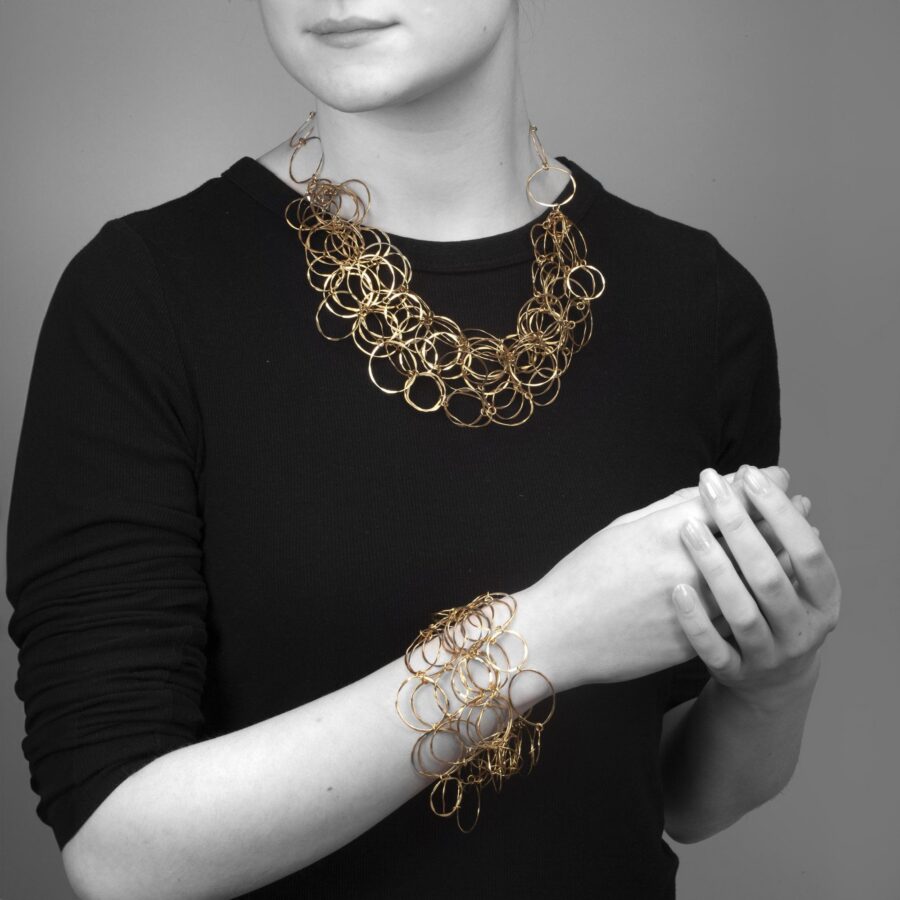An eighteen carat yellow gold necklace with matching bracelet consisting of many strings of irregular round links. Signed Cartier, numbered. Made ca 1980.