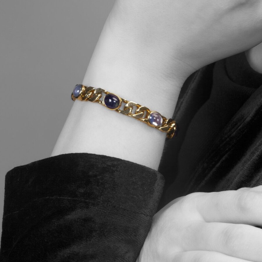 An eighteen carat yellow gold curb chain bracelet, set with six collet set oval cabochon cut blue sapphires. Signed Bvlgari, made ca 1980.