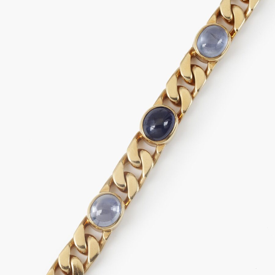 An eighteen carat yellow gold curb chain bracelet, set with six collet set oval cabochon cut blue sapphires. Signed Bvlgari, made ca 1980.