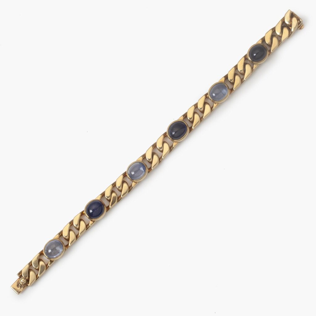 An eighteen carat yellow gold curb chain bracelet, set with six collet set oval cabochon cut blue sapphires. Signed Bvlgari, made ca 1980.