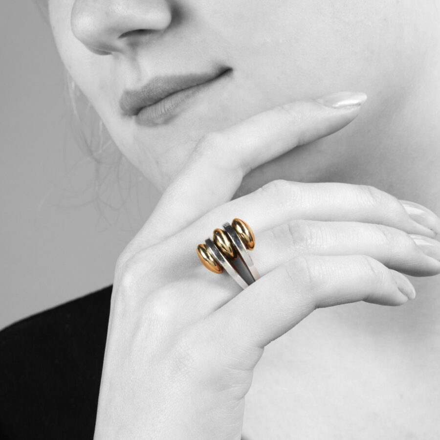 A sterling silver ring with two double convex fourteen carat yellow gold buttons. Signed Pierre Cardin, made ca 1965.