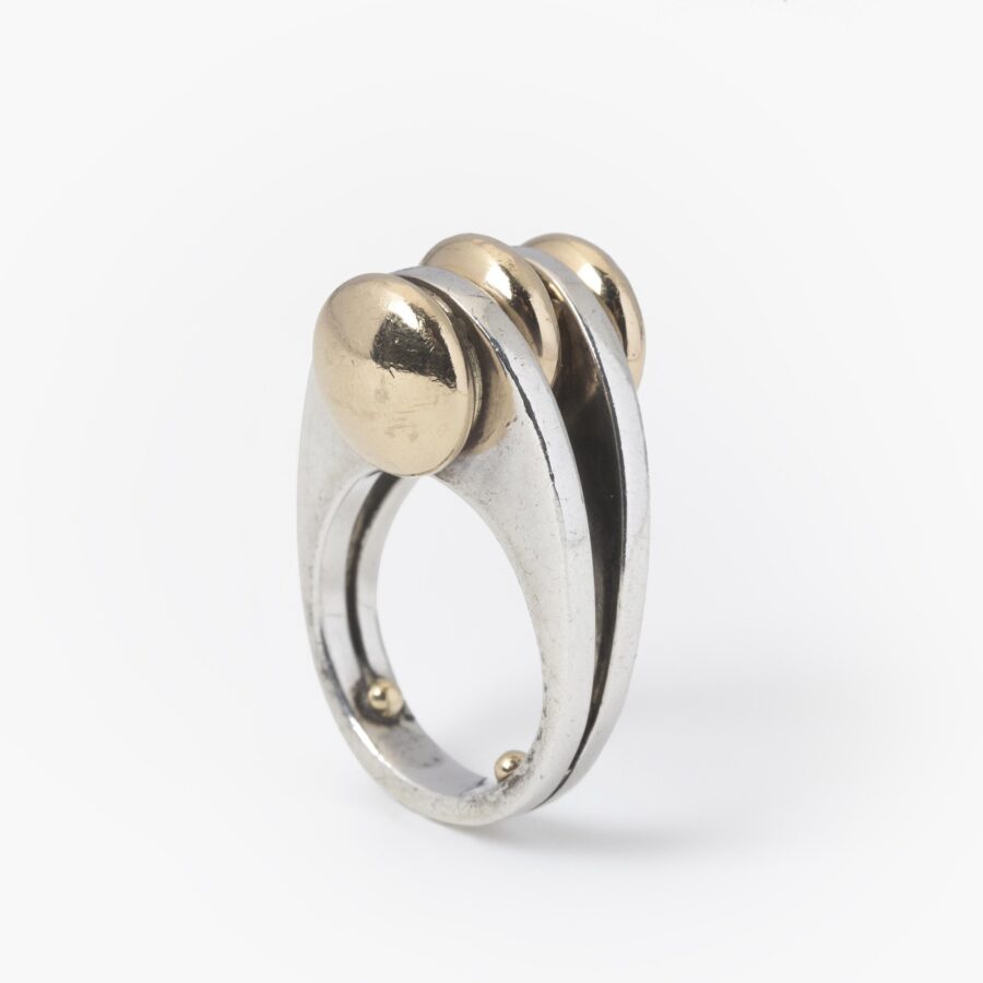 A sterling silver ring with two double convex fourteen carat yellow gold buttons. Signed Pierre Cardin, made ca 1965.
