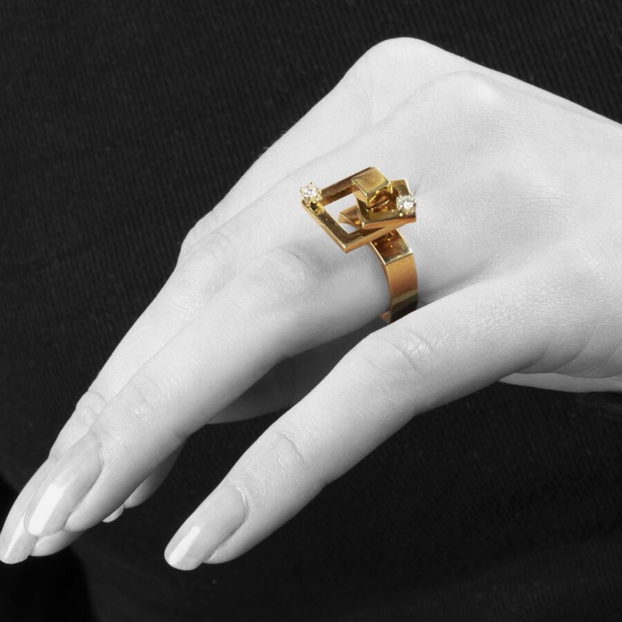 A fourteen carat yellow gold kinetic ring designed as two rotating open squares, each with one diamond. Signed N. Teufel, USA, dated 1972.