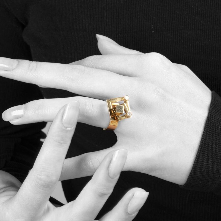 A fourteen carat yellow gold kinetic ring designed as two rotating open squares, each with one diamond. Signed N. Teufel, USA, dated 1972.