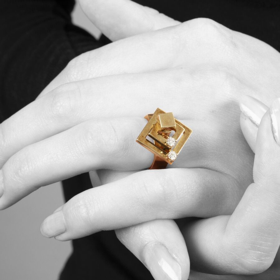 A fourteen carat yellow gold kinetic ring designed as two rotating open squares, each with one diamond. Signed N. Teufel, USA, dated 1972.